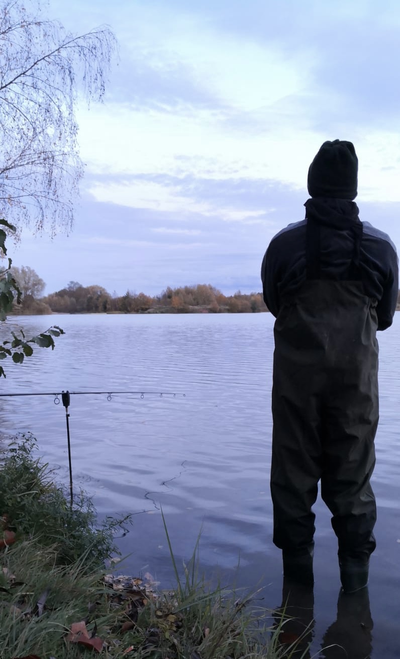 Angler in Wathose am Ufer, davor eine Rute mit Bissanzeiger