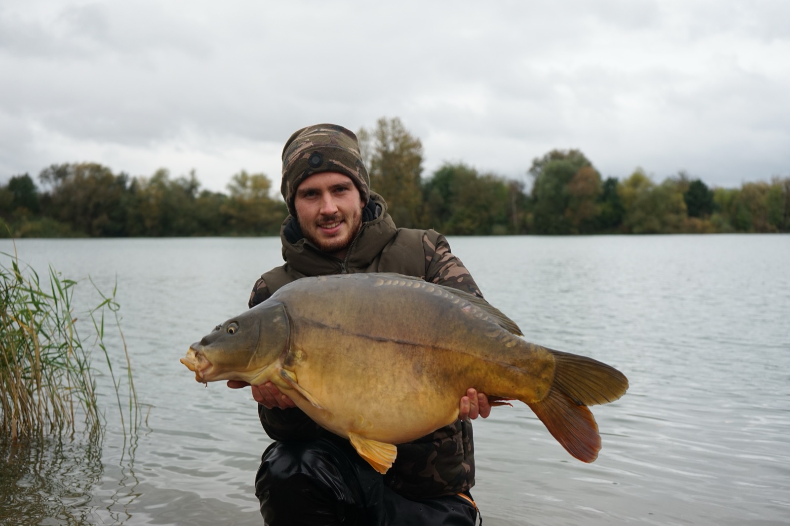 Fabi mit einem großen Spiegelkarpfen im Wasser stehend, Herbstwetter